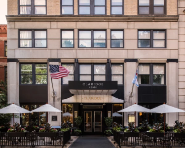The image shows the entrance of a building with "CLARIDGE HOUSE" signage, flanked by American and state flags, and outdoor seating with umbrellas.