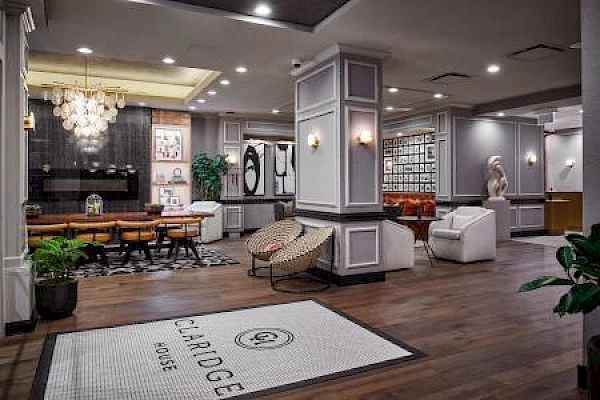 A stylish hotel lobby with modern furniture, artwork, and a chandelier. The floor features a mat with "Claridge House" written on it.