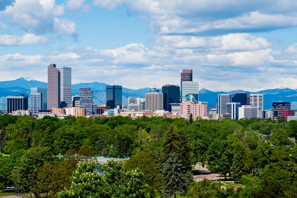 A city skyline with skyscrapers set against a backdrop of mountains and a partly cloudy sky, and a lush green foreground.