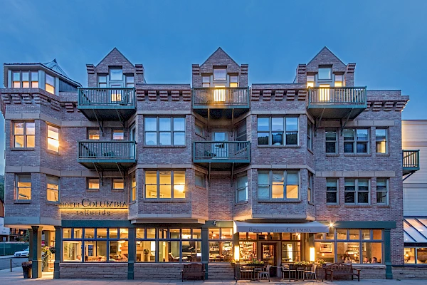 This image shows a three-story brick building with lit windows and balconies, likely a hotel or apartment complex, taken during twilight hours.