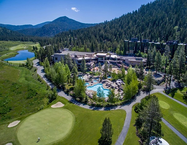 The image shows a resort surrounded by forested mountains and a golf course, with a swimming pool and multiple buildings nestled among trees.