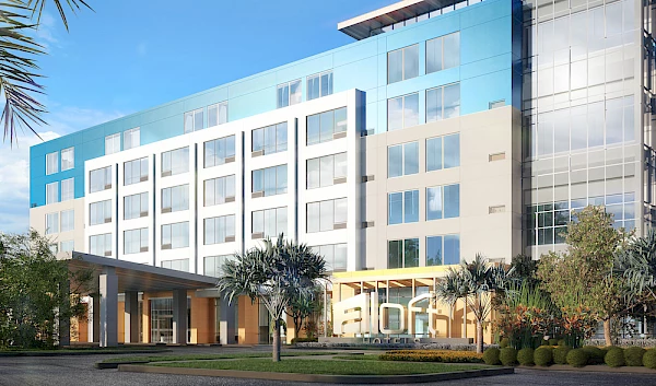 This image shows a modern hotel building with a sleek, contemporary design, featuring large windows and a well-maintained entrance with landscaping.