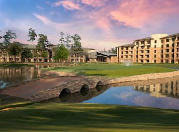 The image shows a serene landscape with a body of water, a stone bridge, and a multi-story building under a colorful sky at sunset.