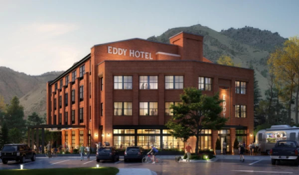 A red-brick building labeled "Eddy Hotel" stands amidst a scenic mountain backdrop, with cars parked in front and people walking around the area.