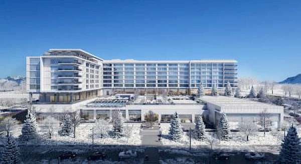 A modern mid-rise building, possibly a hotel or resort, is surrounded by snow-covered trees and landscape under a clear blue sky.